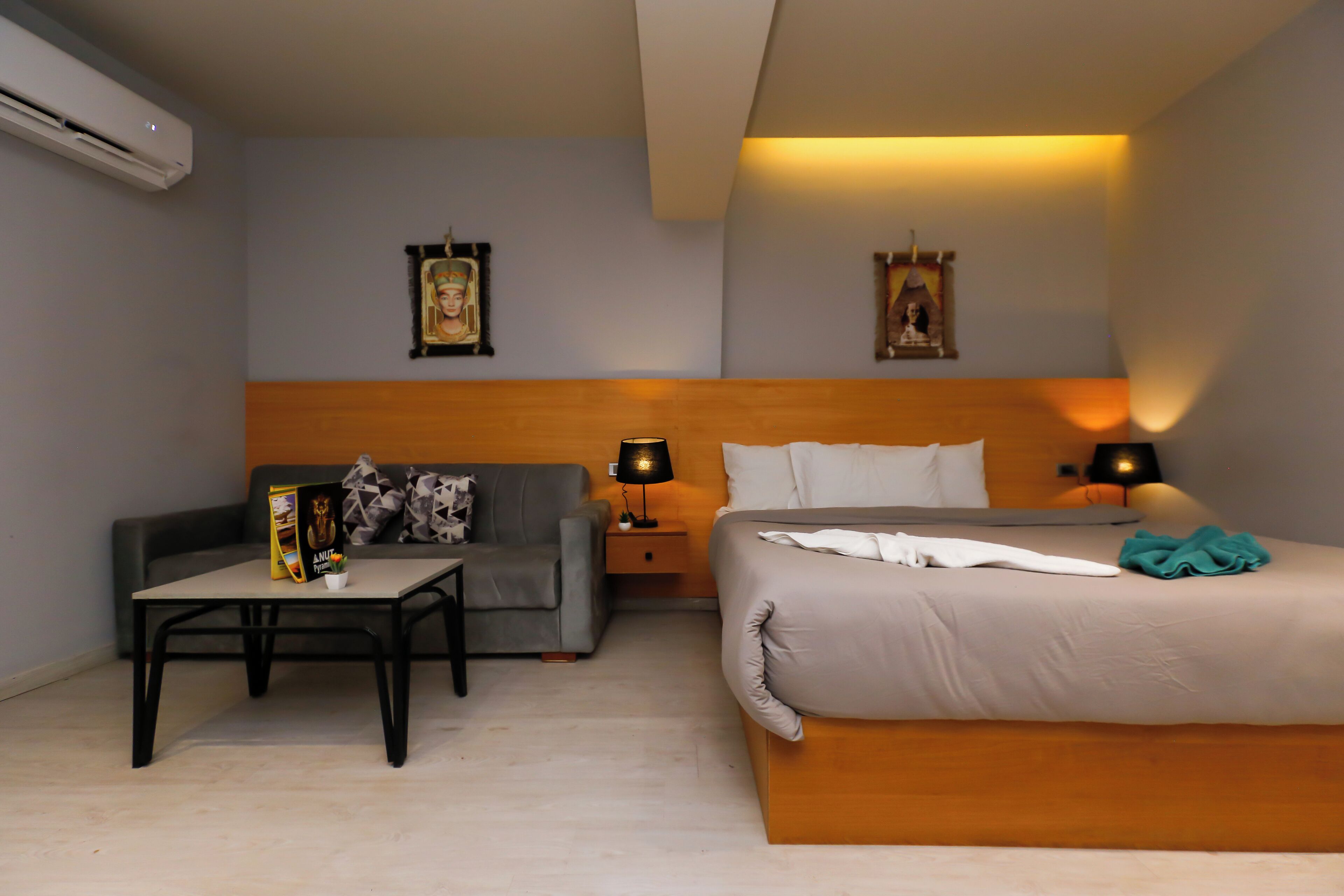 A hotel room with a bed, a sofa, a small table, and two wall-mounted lamps.