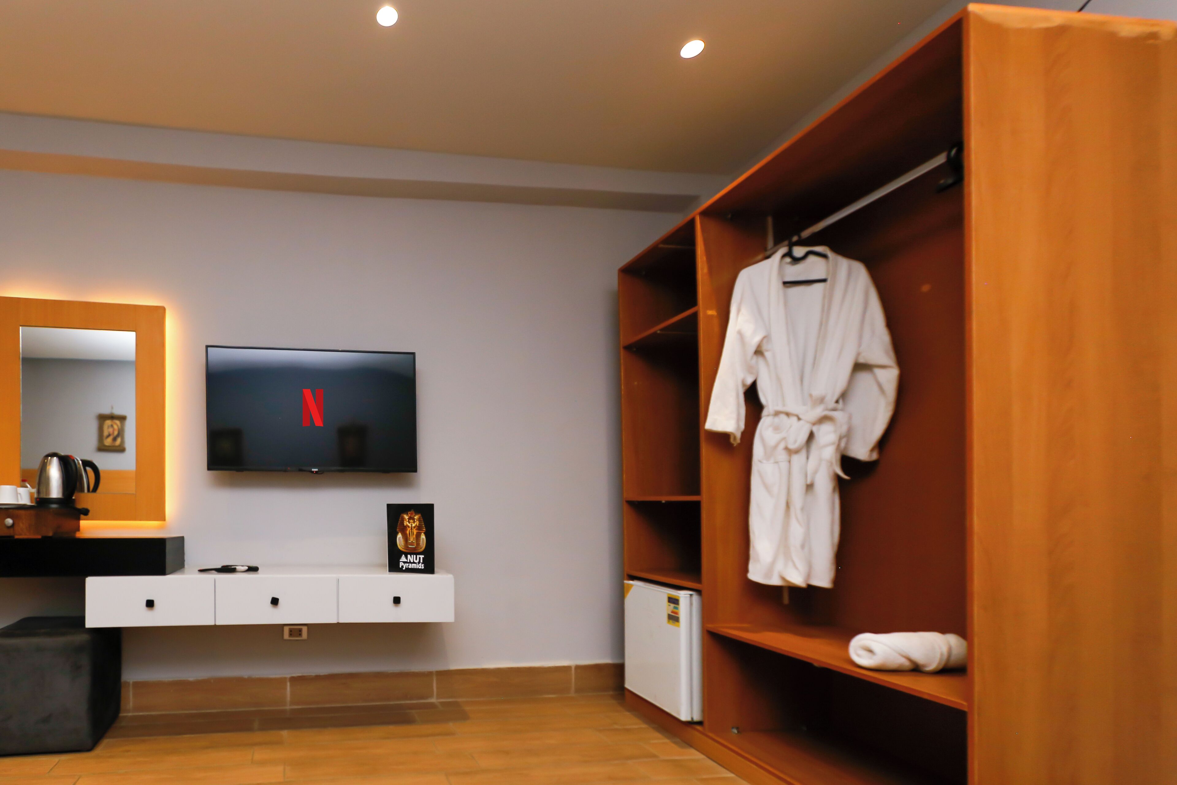 A modern bathroom with a wooden vanity, a flat-screen TV, and a robe hanging on a rack.