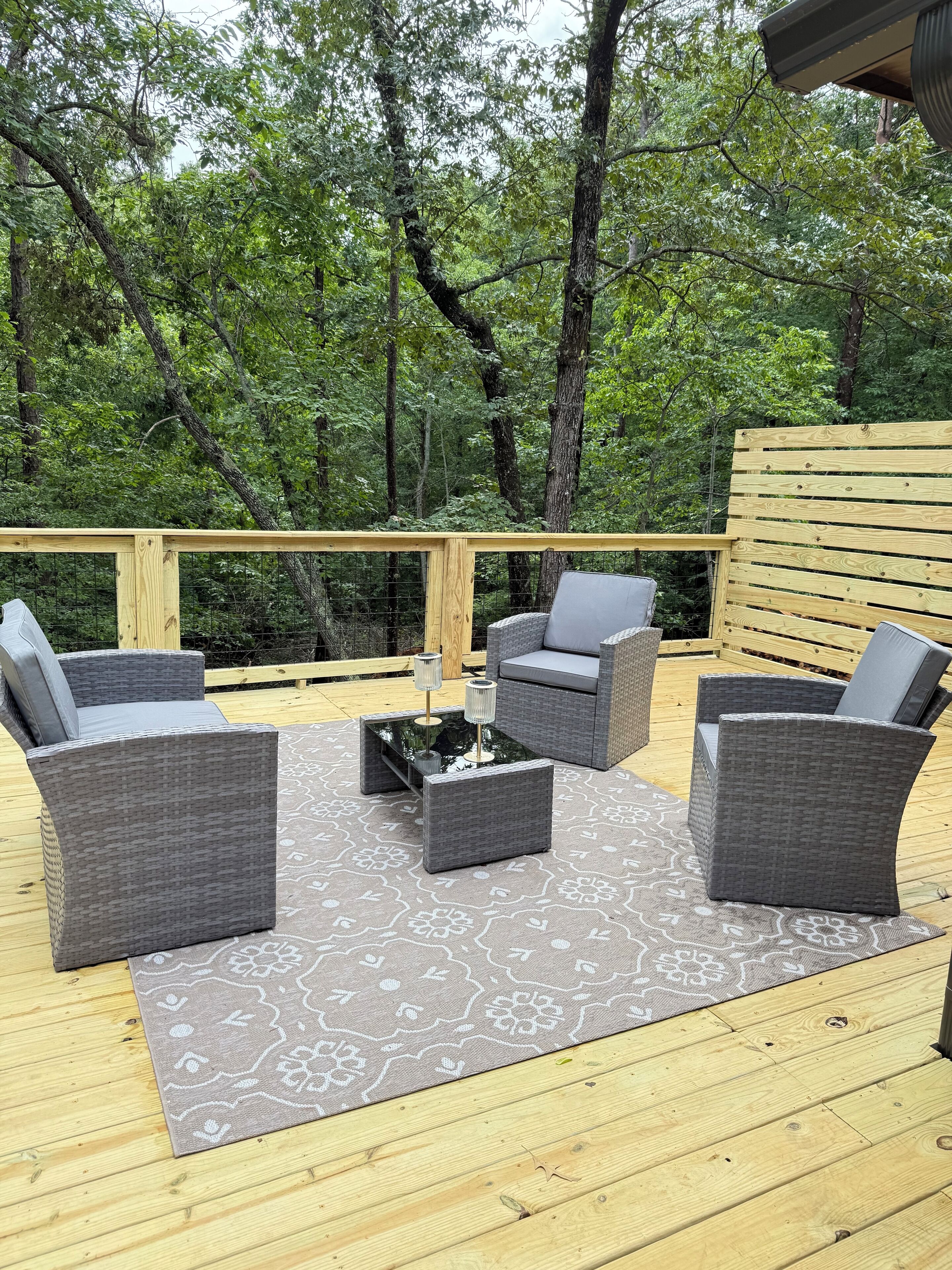 A deck with wicker furniture and a patterned rug.