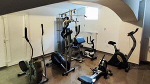 Een sportschool met diverse fitnessapparaten, een bank en een raam dat voor natuurlijk licht zorgt.