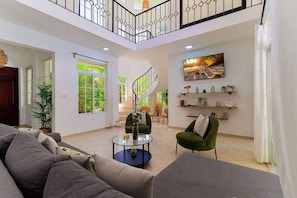 Un vaste espace de vie comprenant un escalier, un fauteuil vert, un canapé et une table basse.