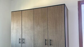 A large wardrobe with two doors and a handle, placed in a room with white walls and a tiled floor.