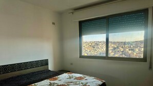 A bedroom with a bed, a window with a city view, and a decorative headboard.