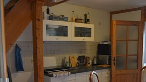 Une cuisine avec des poutres en bois, des meubles blancs, une table à manger avec des chaises et un escalier en bois.