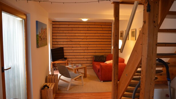 Un salon chaleureux avec un plancher en bois, un canapé rouge, un meuble TV en bois et un escalier.