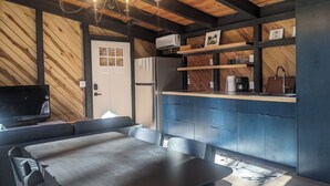 A modern kitchen with a built-in refrigerator, a coffee machine, and a sink. There is a dining area with a table and chairs, and a television on the left.