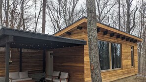 A wooden cabin with a covered patio area, two chairs, and a small table.
