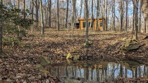 A rustic cabin surrounded by a forest with a small pond in the foreground.
