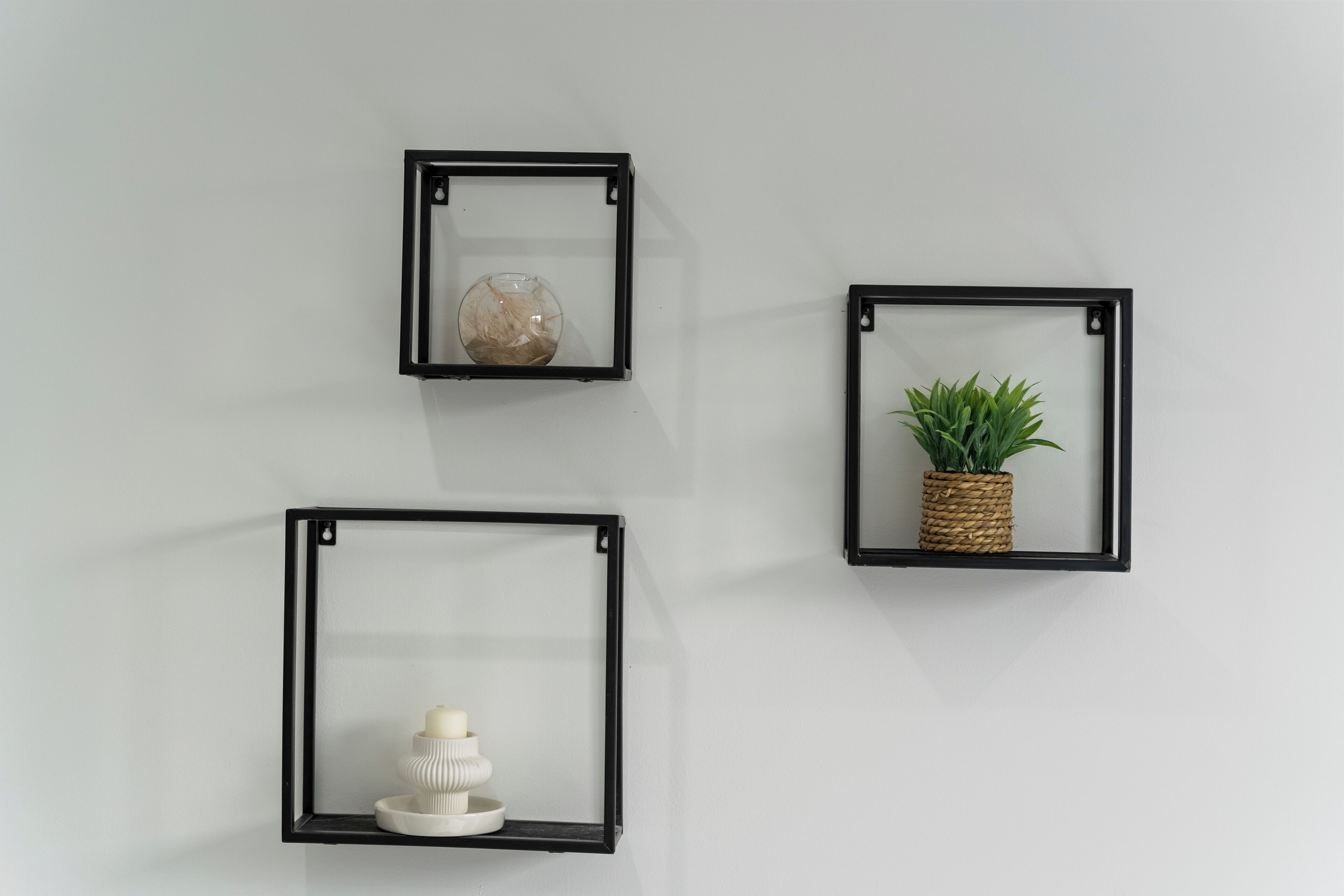 Drie zwarte wandplanken tegen een effen muur, elk met verschillende decoratieve objecten.