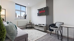 A modern living room with a grey sofa, a small round table, a TV mounted on the wall, and a window with a city view. - City Centre Luxury ApartmentSofa BedWIFI (Leicester)