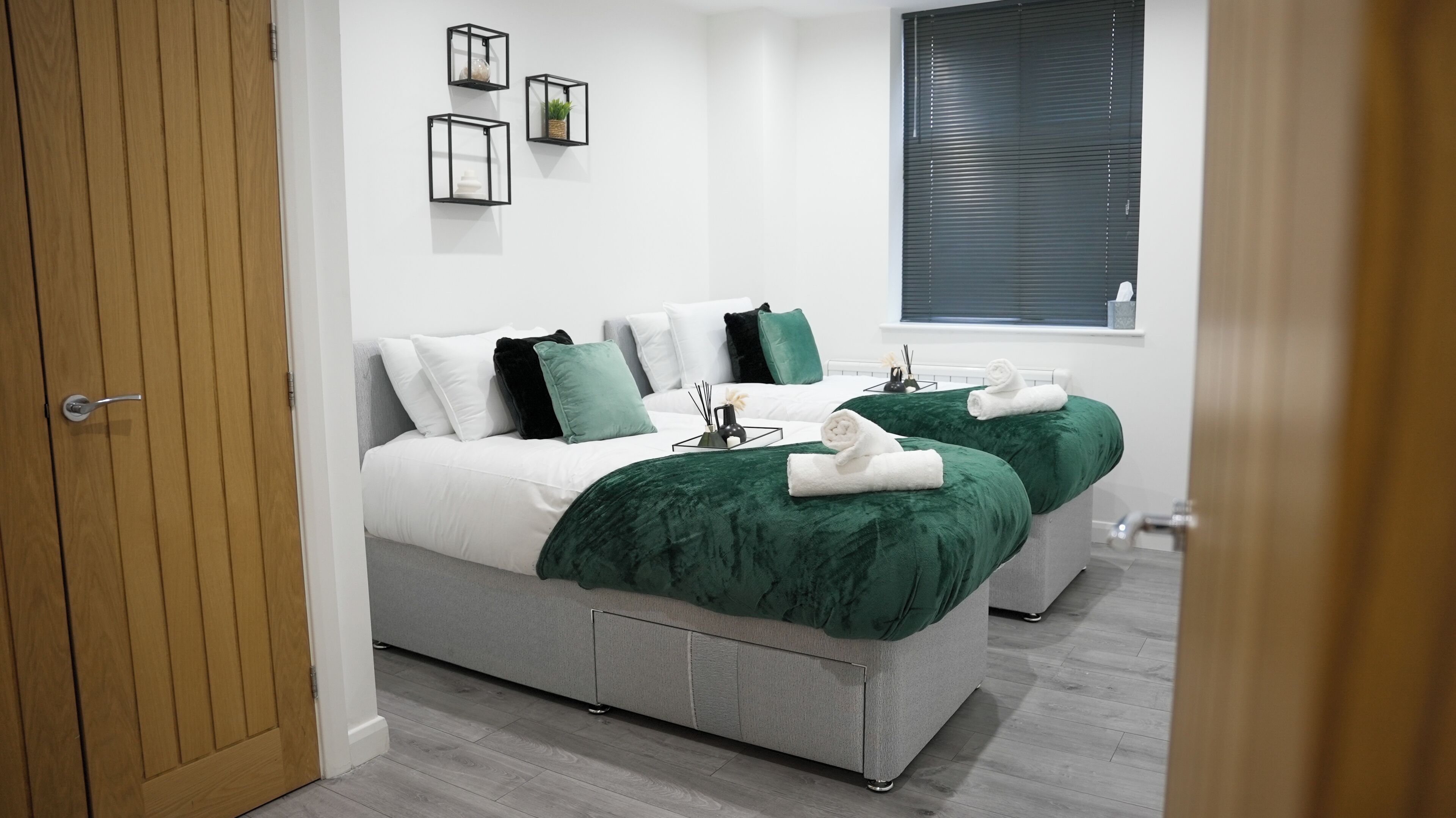 A modern bedroom with two beds, a window, and a door.