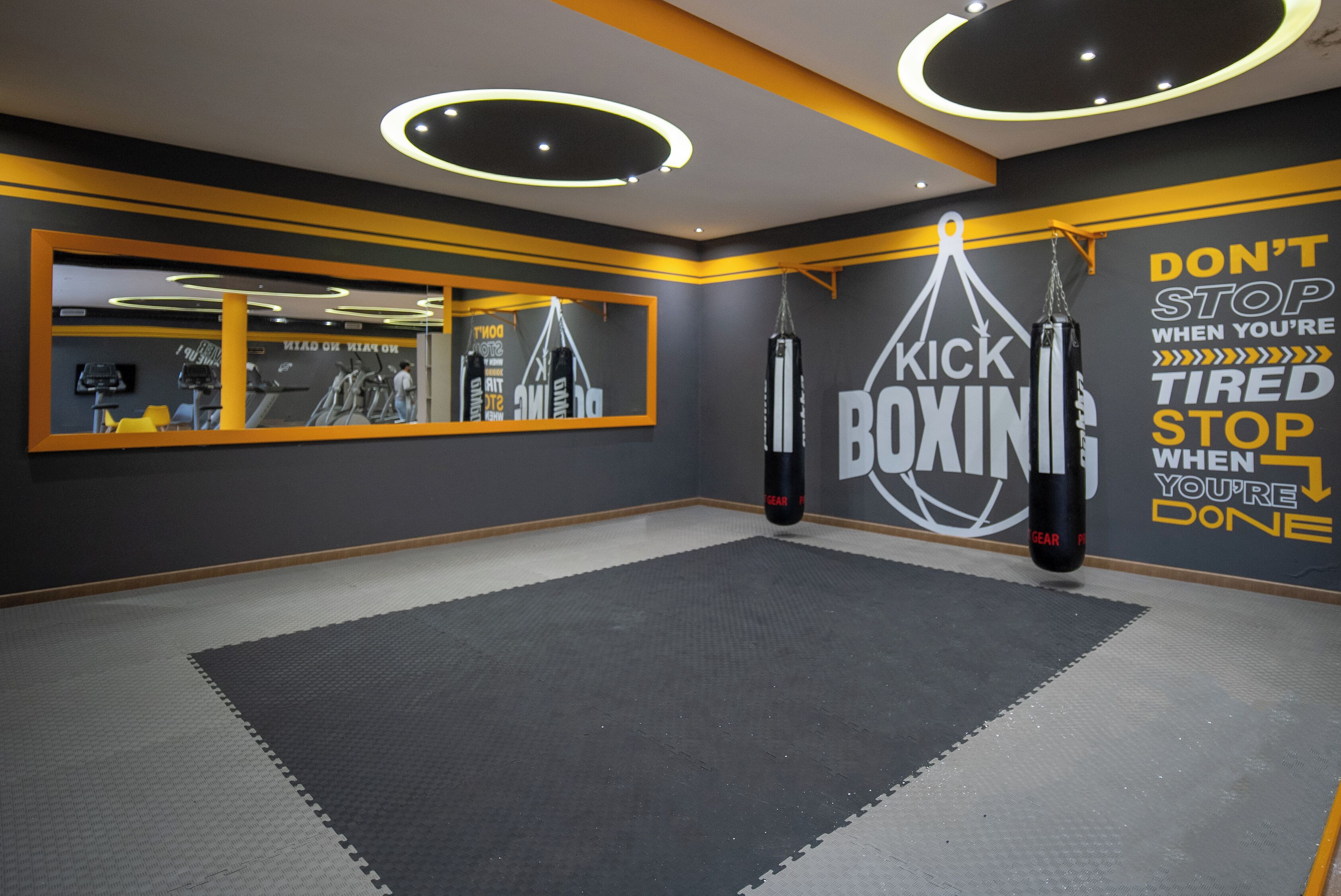 A gym with a mirrored wall, punching bags, and motivational wall art.