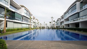 Een modern hotel met een centraal gelegen zwembad, diverse balkons en palmbomen.