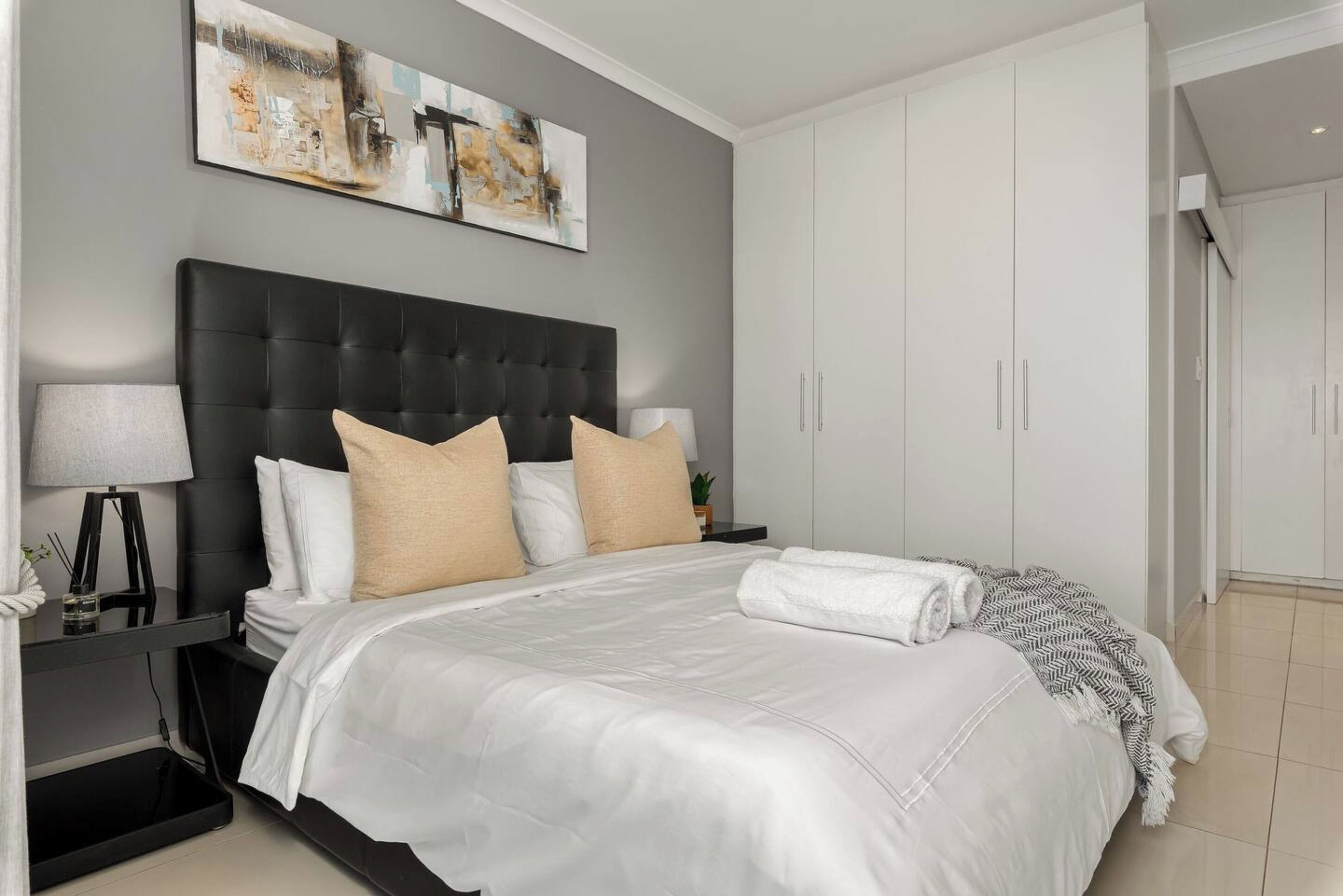 A modern bedroom with a large bed, a nightstand, a lamp, and a wardrobe.