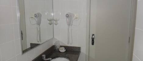 A bathroom with a sink, two hair dryers mounted on the wall, and a door with a lock.