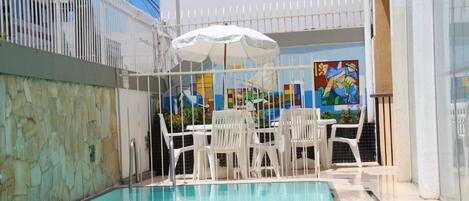 Una piscina interior con sillas blancas y una sombrilla, rodeada por una valla blanca y un mural en la pared.
