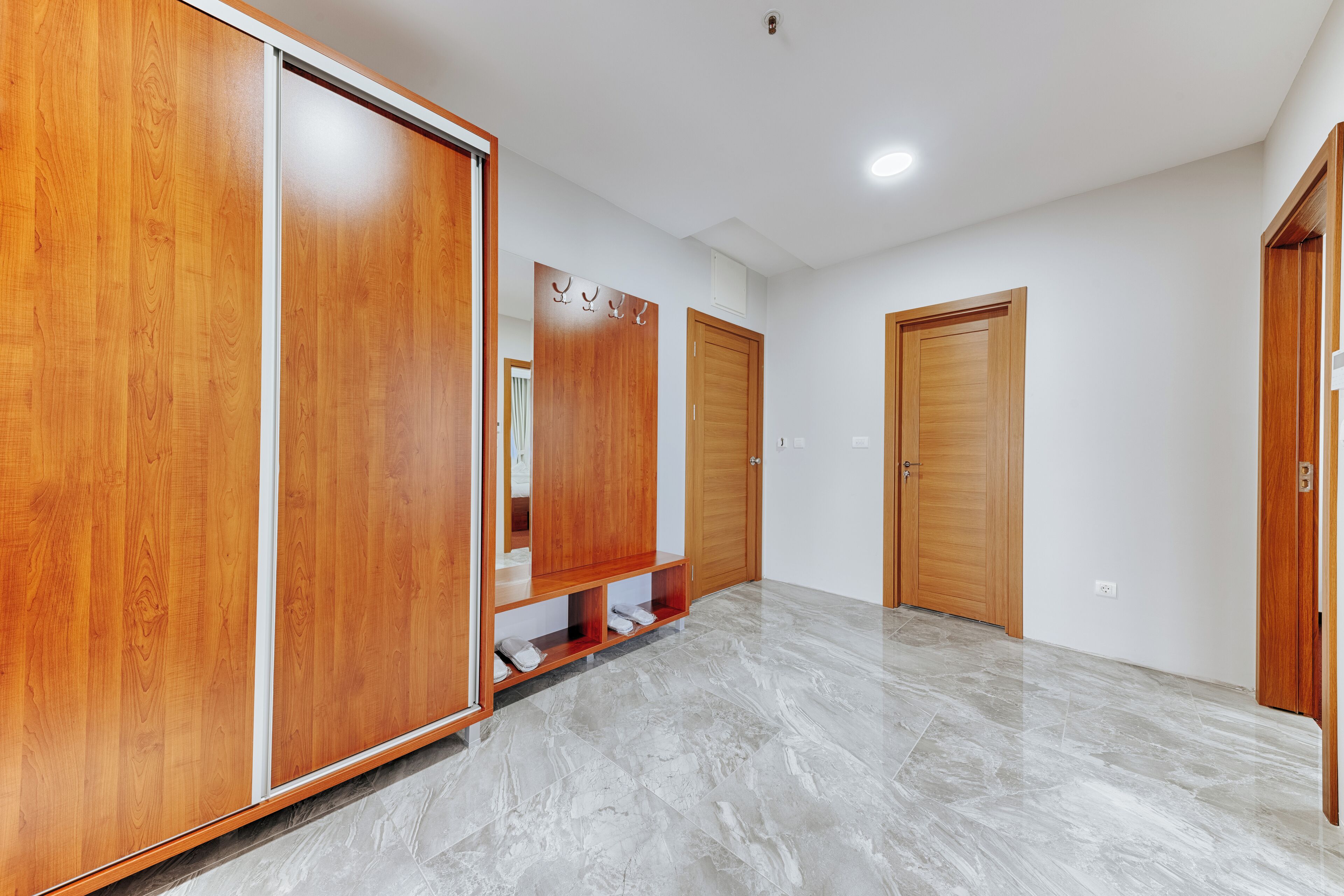 A hallway with wooden wardrobes, a marble floor, and a white wall.