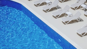 Zona de piscina con sillas reclinables blancas y sombrillas, rodeada por una valla baja.