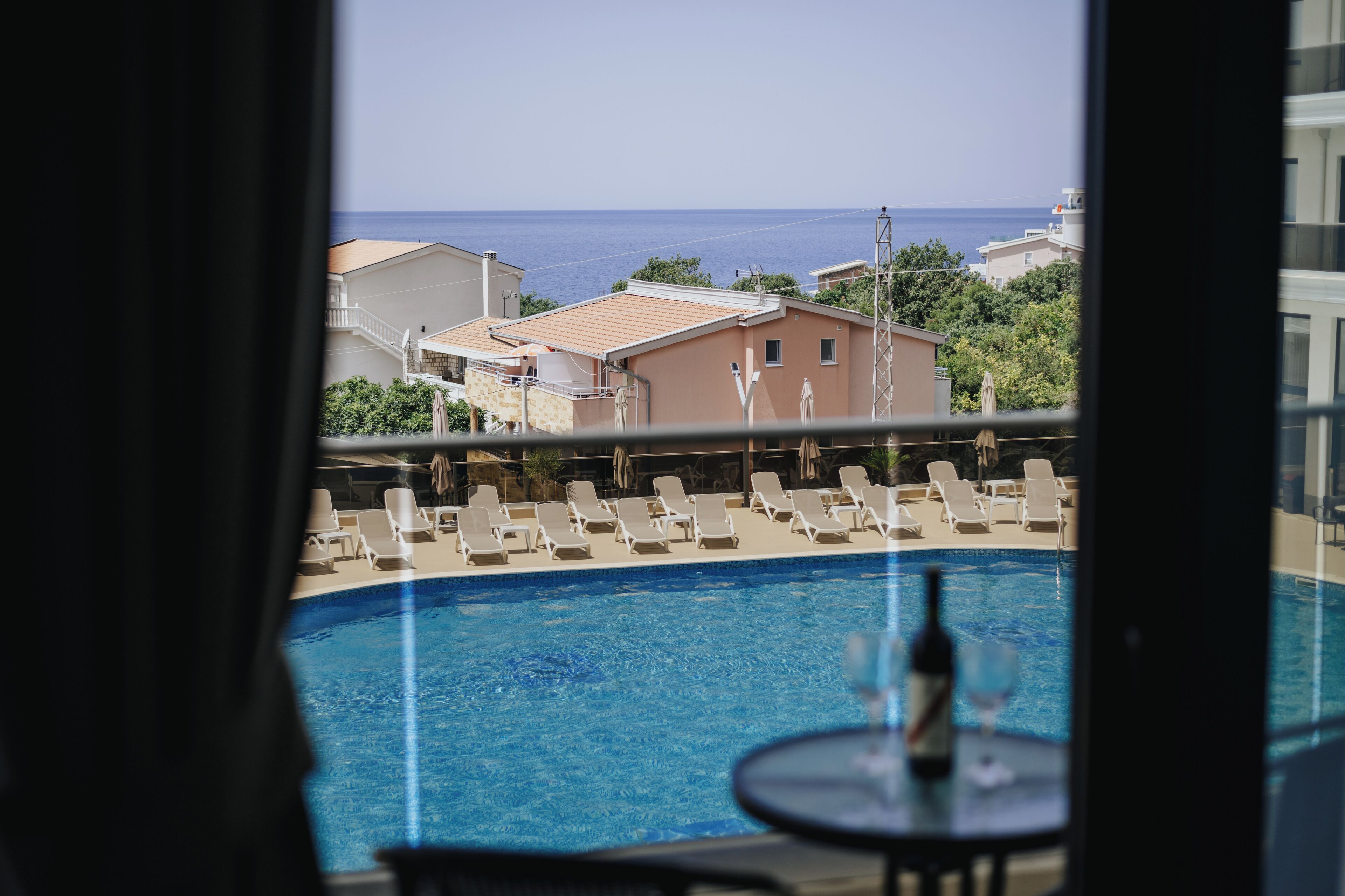 A poolside view with lounge chairs and a table, overlooking a residential area and the sea.