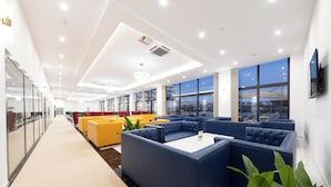 A modern lounge area with blue and yellow seating, large windows, and a city view. - Casa Costa (Bar)