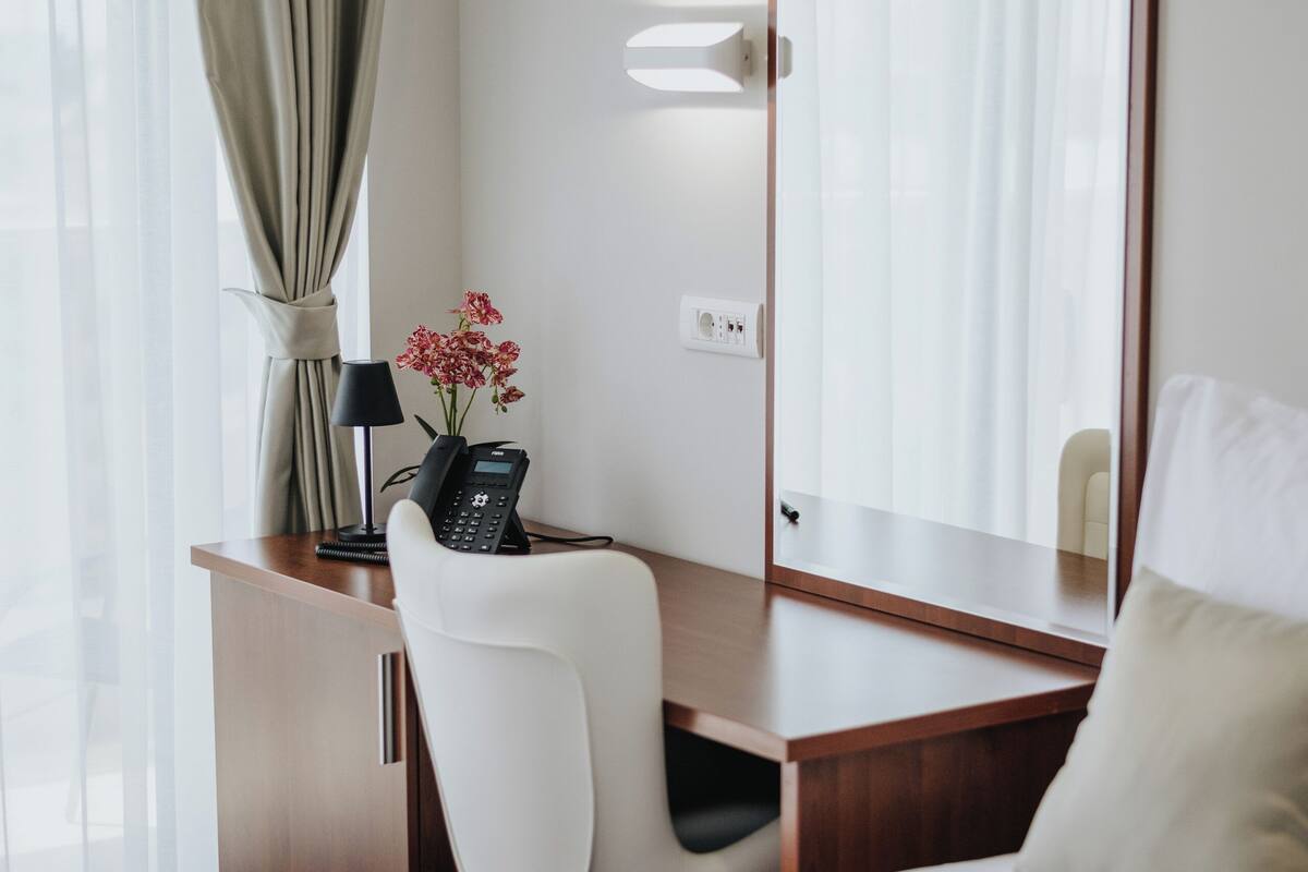 A hotel room with a bed, a desk with a telephone, a chair, a lamp, and a mirror.