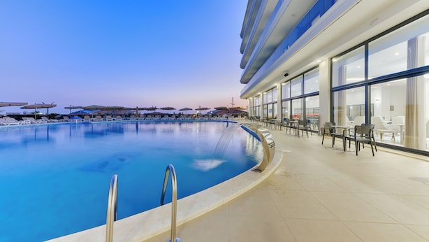 A swimming pool with lounge chairs and tables, surrounded by a building with large windows. - Casa Costa (Bar)