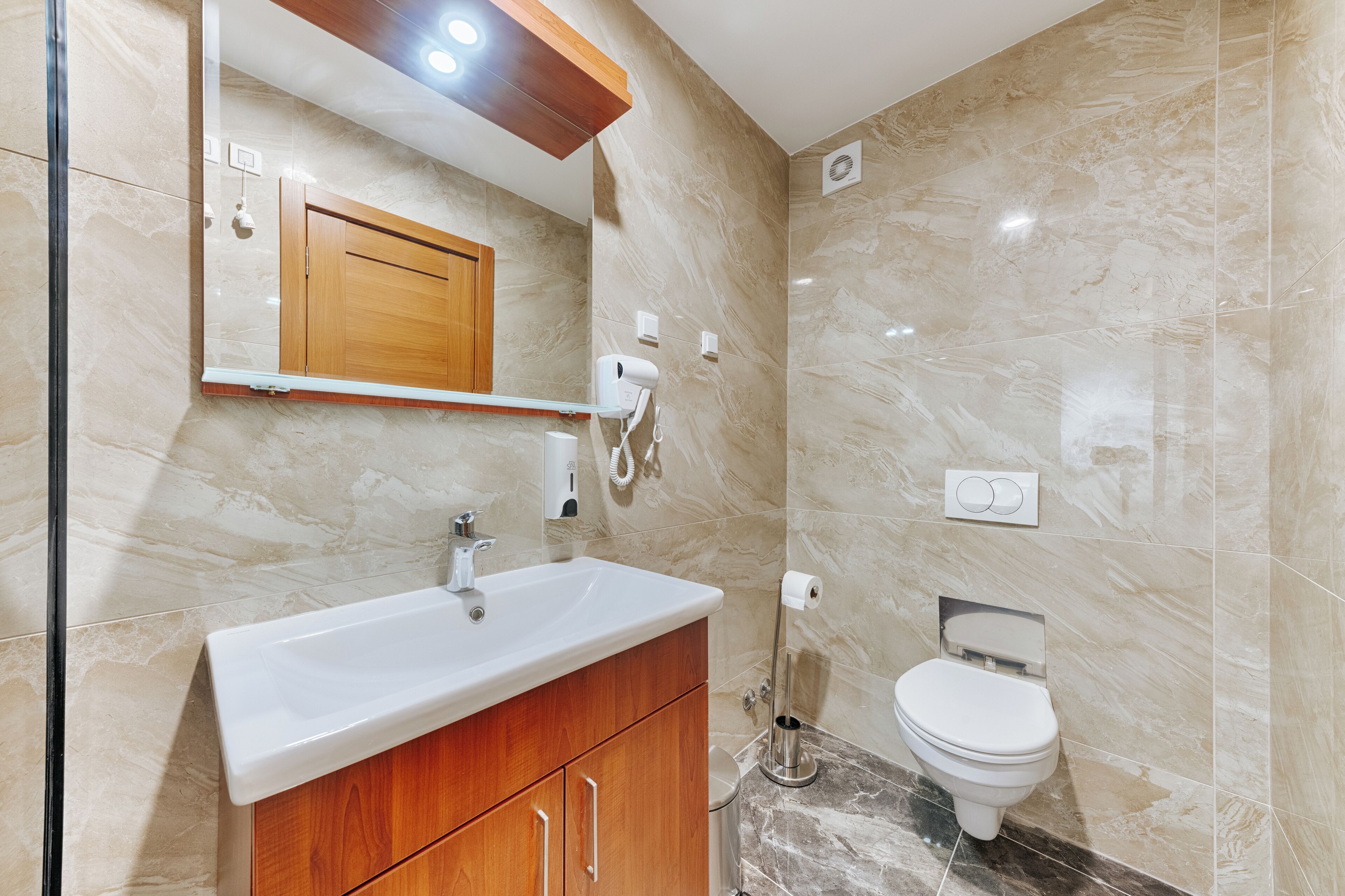 A bathroom with a marble sink, wooden cabinets, a mirror, a hairdryer, and a toilet.