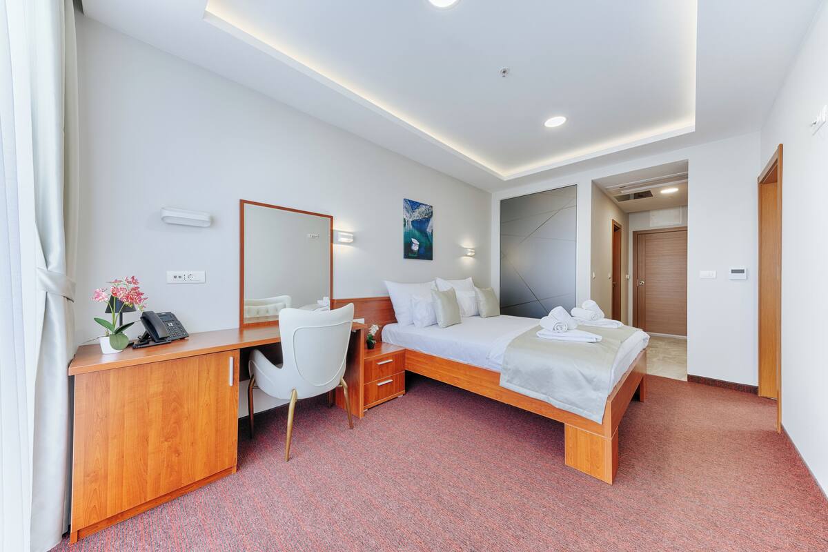 A hotel room with a wooden desk, a bed, a chair, and a large mirror.