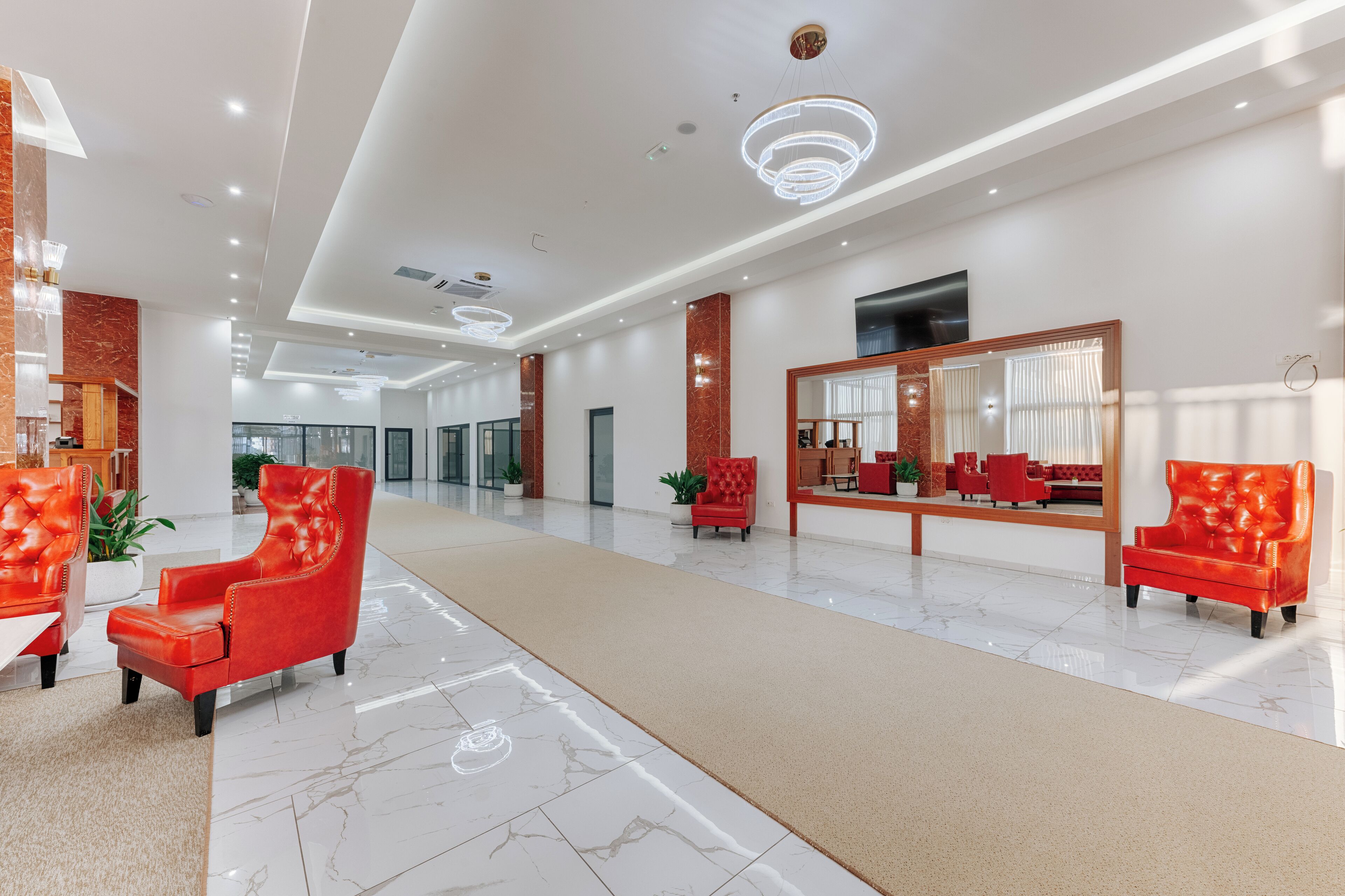 A spacious lobby with a marble floor, red leather chairs, a large mirror, and modern lighting fixtures.