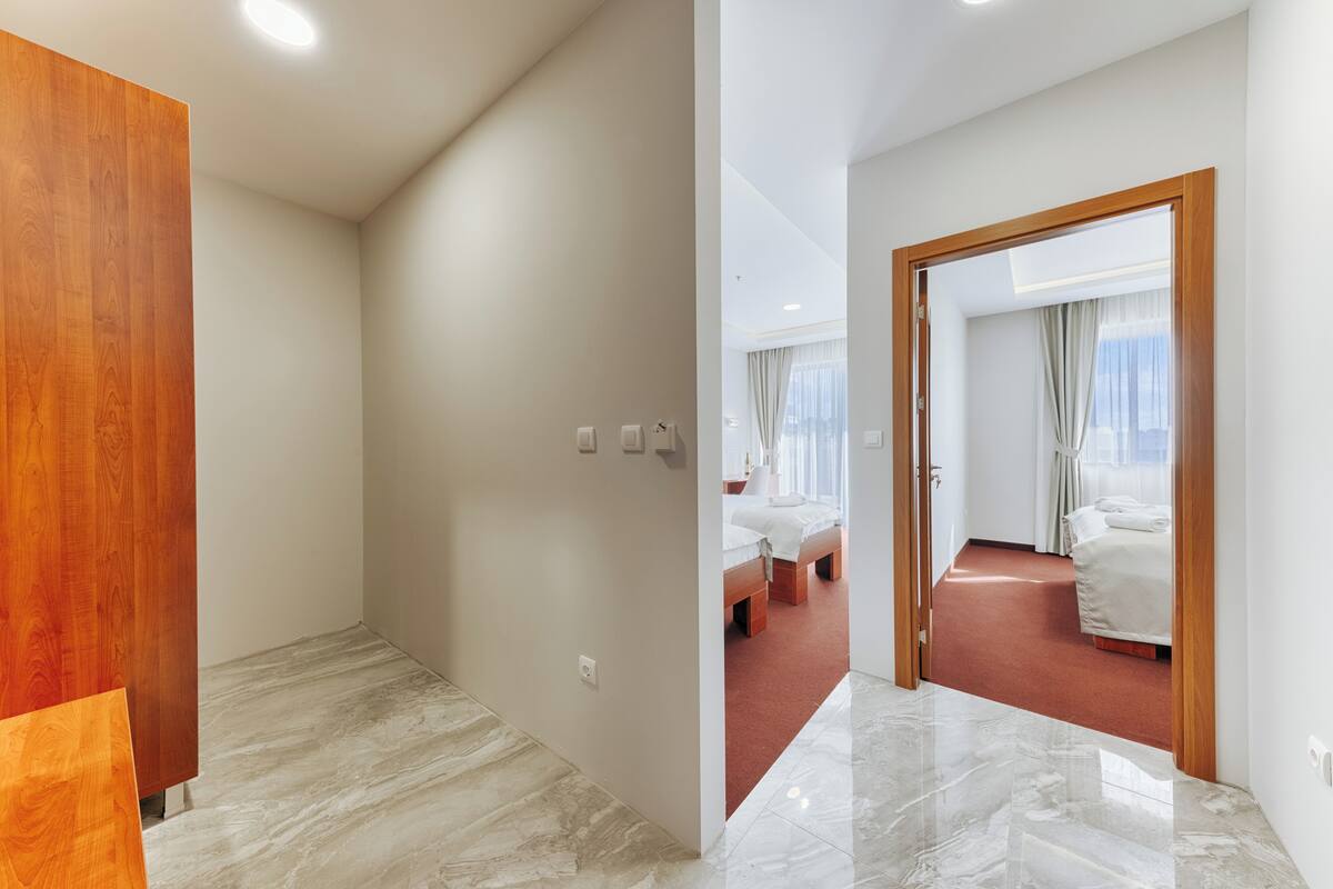 A hotel room with a wooden wardrobe, a marble floor, and a bed with white bedding.