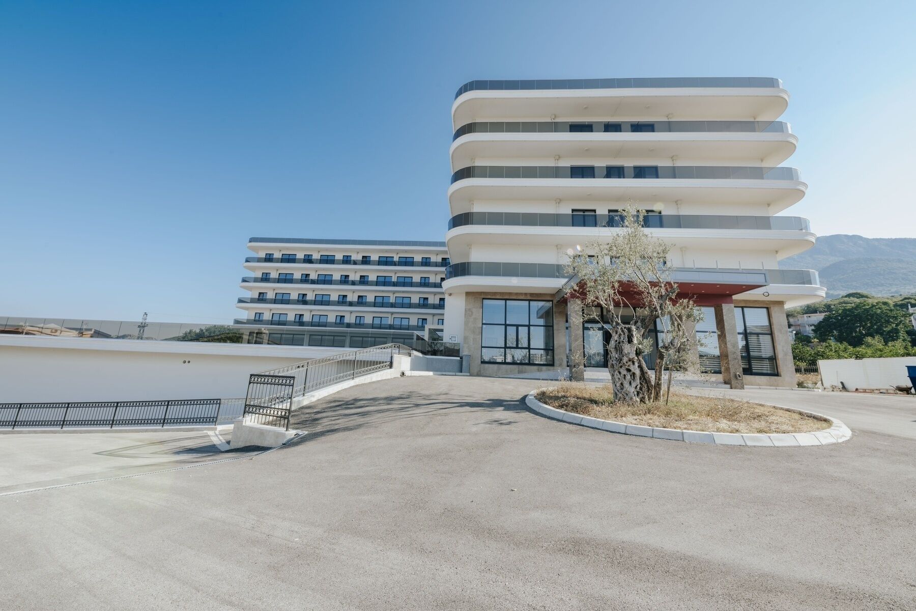 Un hotel moderno de varios pisos con fachada curva, amplias ventanas y una entrada central con zona cubierta.