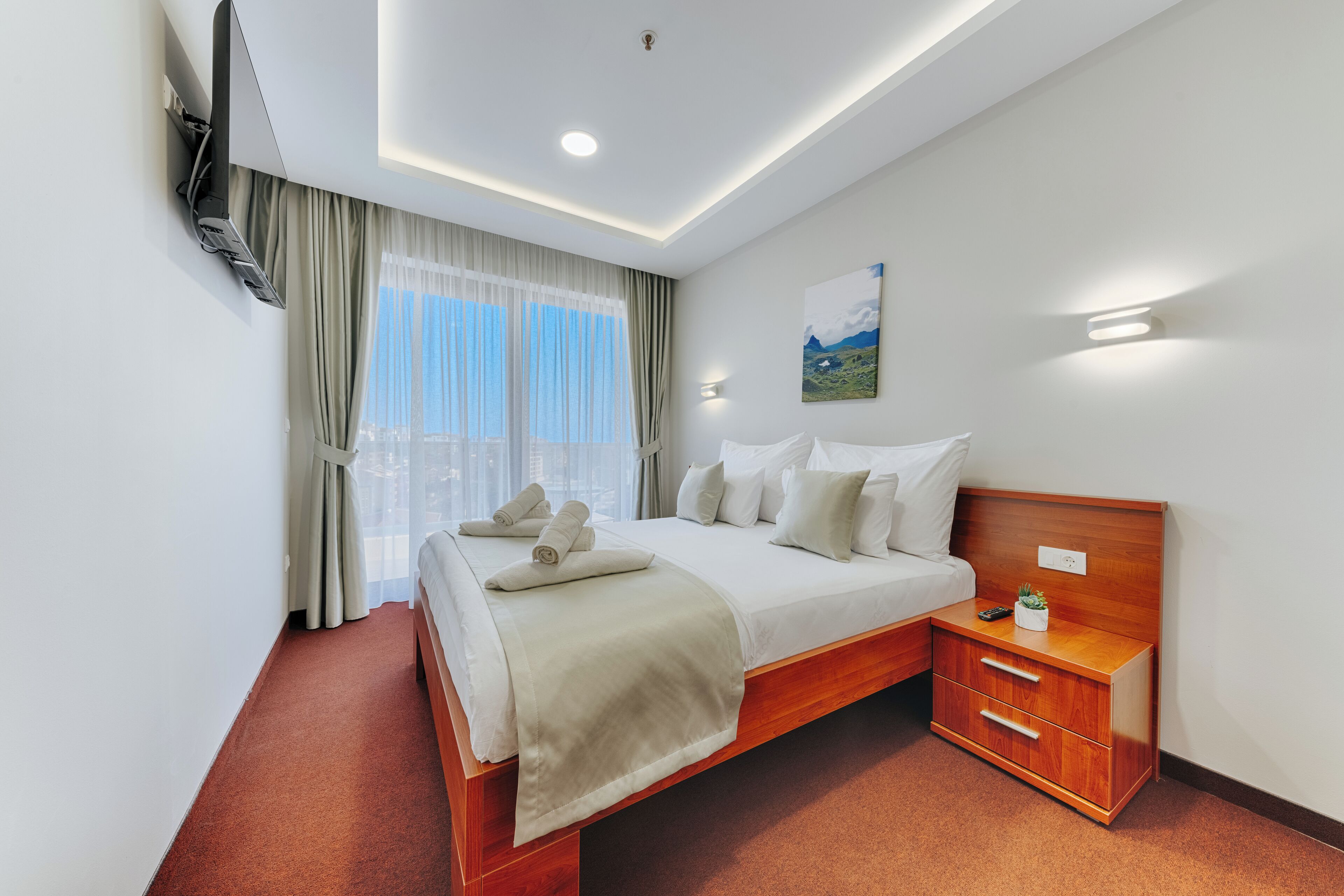 Una habitación de hotel con cama, mesita de noche y televisor montado en la pared.