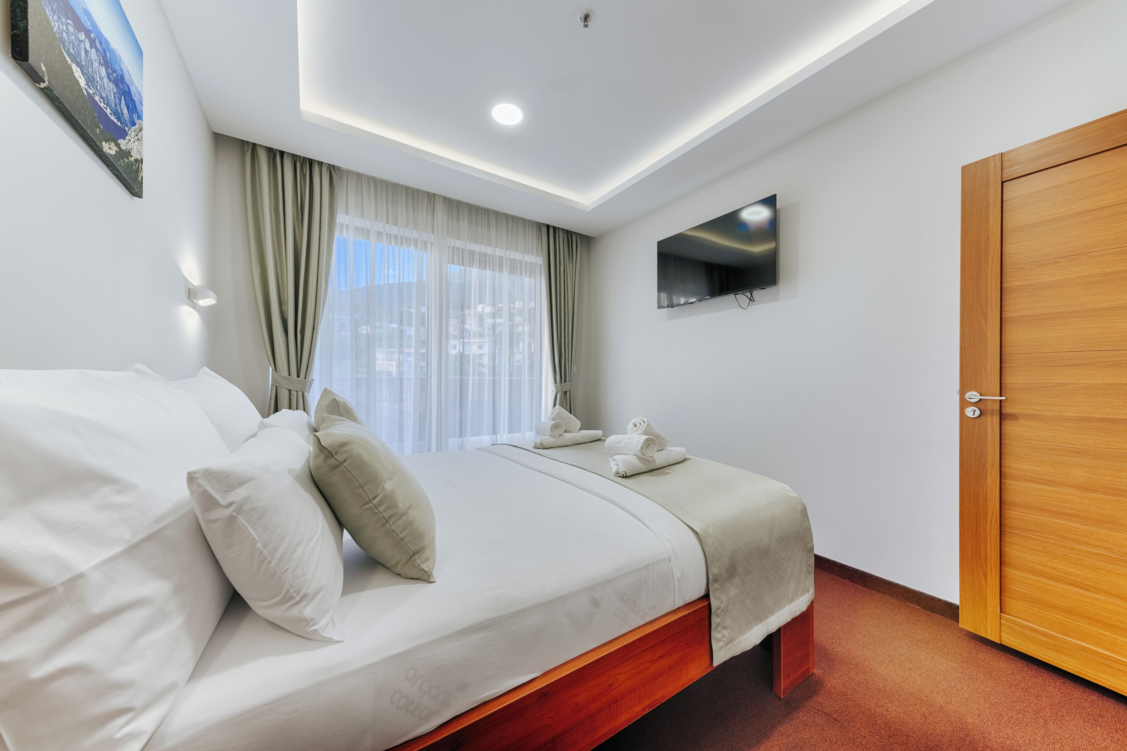 A hotel room with a bed, a TV mounted on the wall, and a wooden door.