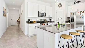 Una cocina moderna con armarios blancos, una isla central con taburetes, electrodomésticos de acero inoxidable y un reloj en la pared.
