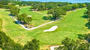 Campo de golf con búnkeres de arena, árboles y una vista despejada del agua.