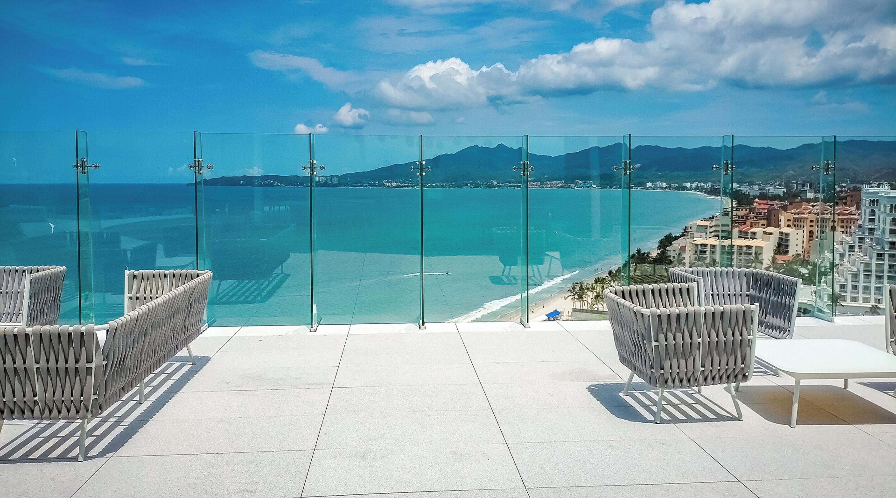 A balcony with glass railings overlooking a beach and cityscape.