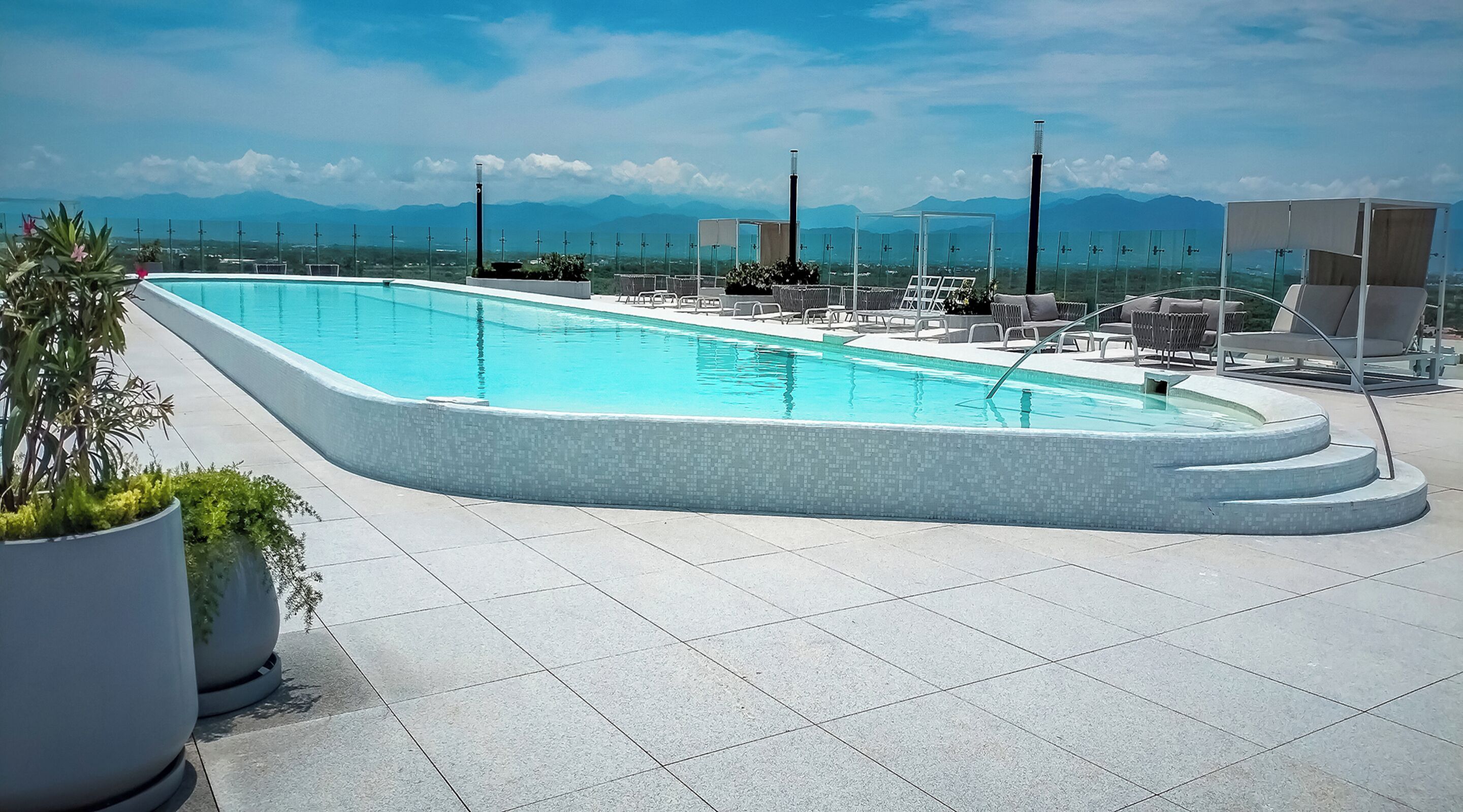 A rectangular pool with a tiled edge, surrounded by lounge chairs and potted plants.