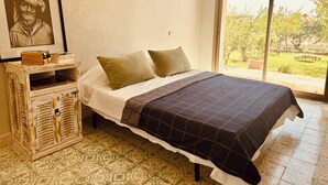 Une chambre à coucher avec un lit, une commode, un tableau encadré et une vue sur l’extérieur.