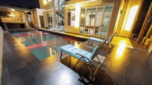 Une piscine avec des chaises longues, un mur en pierre et un bâtiment moderne doté de grandes fenêtres.