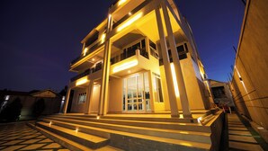 Un bâtiment moderne avec un escalier menant à l’entrée, de grandes portes vitrées et des marches éclairées.