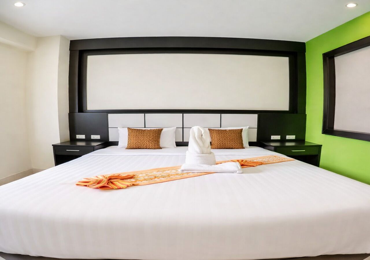 Habitación de hotel con una cama grande, dos mesitas de noche, un cabecero y una pared verde decorativa.