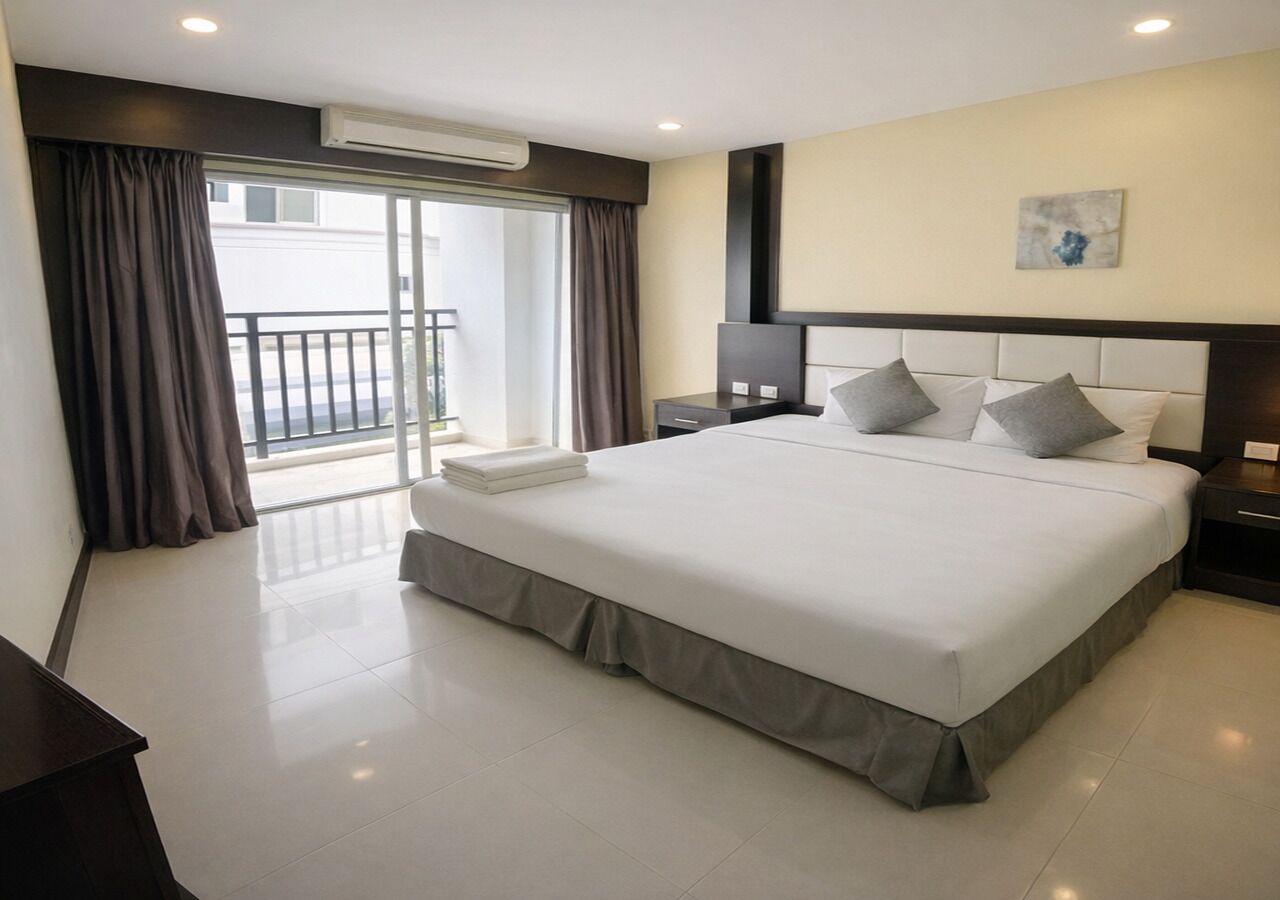 A hotel room with a large bed, a bedside table, a nightstand, and a view of the outside through a sliding door.