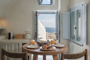 A dining table with plates, glasses, and a kettle, overlooking a scenic view. - Lunar Sea Suite Hot-tub & Caldera View (Santorini)