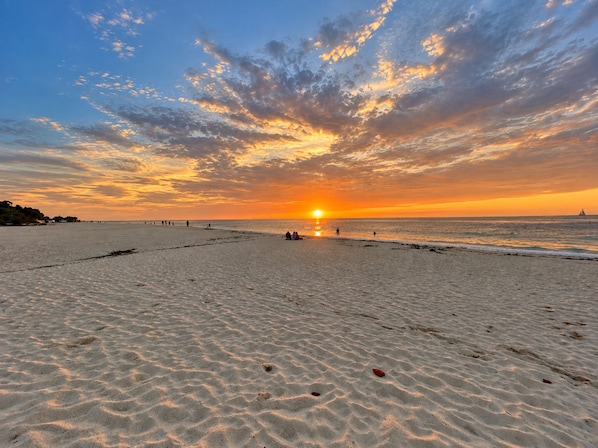 A beach with a sunset, sand, and a distant sailboat.