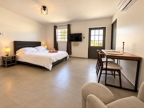 Habitación de hotel con cama, mesita de noche, lámpara, televisor, escritorio, silla y una puerta.