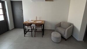 Ett litet, modernt rum med ett matbord i trä, två stolar, en grå pall, en grå fåtölj och en väggmonterad luftkonditioneringsanläggning.