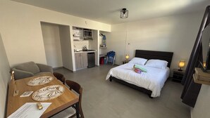 Ett kompakt hotellrum med en säng, sängbord, ett litet pentry och en matplats med ett bord och stolar.