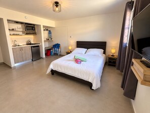 Een hotelkamer met een bed, nachtlampjes, een televisie, een kitchenette met een magnetron, en een zithoekje.