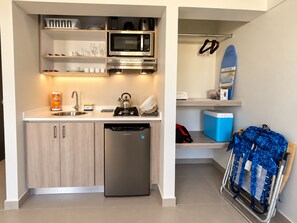 Una kitchenette compacta equipada con microondas, hervidor y escurreplatos.