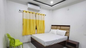 A bedroom with a bed, a chair, a nightstand, and an air conditioning unit. - Shekhar Palace (Varanasi)